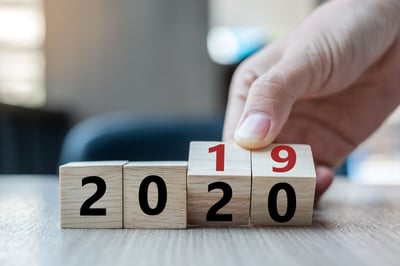 Business man hand holding wooden cube with flip over block 2019 to 2020 word on table background.
