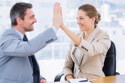 Smartly dressed young man and woman giving high five in a business meeting at office desk