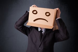 Businessman standing and gesturing with a cardboard box on his head with sad face