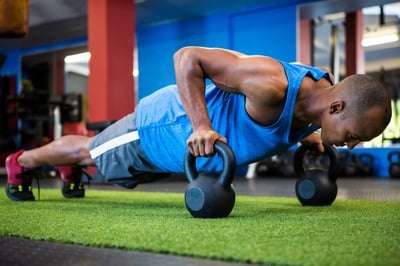 Full length of male athlete doing push-ups with kettlebells in fitness studio