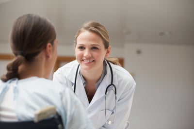 Smiling doctor looking at a patient on a wheelchair in hospital hallway