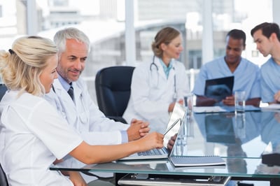 Two smiling doctors using laptop in front of medical team