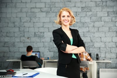Young happy businesswoman with arms folded standing in office