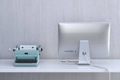 An old fashioned typewriter next to a modern monitor.